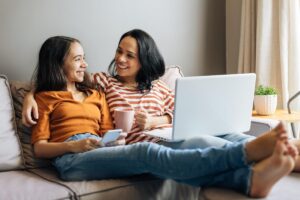 a young person sitting on the couch with their parent who is hugging them while they look at a computer screen