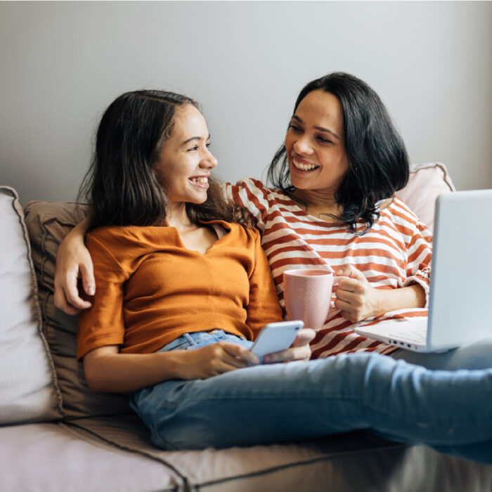 a young person sitting on the couch with their parent who is hugging them while they look at a computer screen