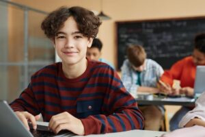 a teen looks at a laptop and smiles at the camera after learning About Inward Healthcare