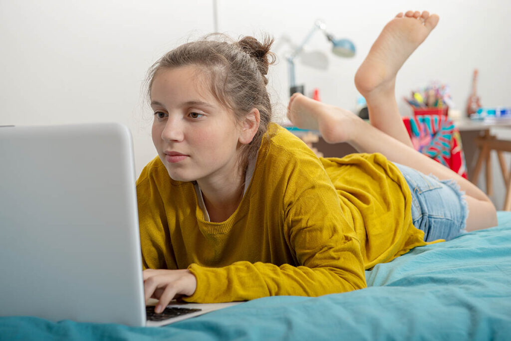 a teen lays on their bed looking at their laptop for OCD help