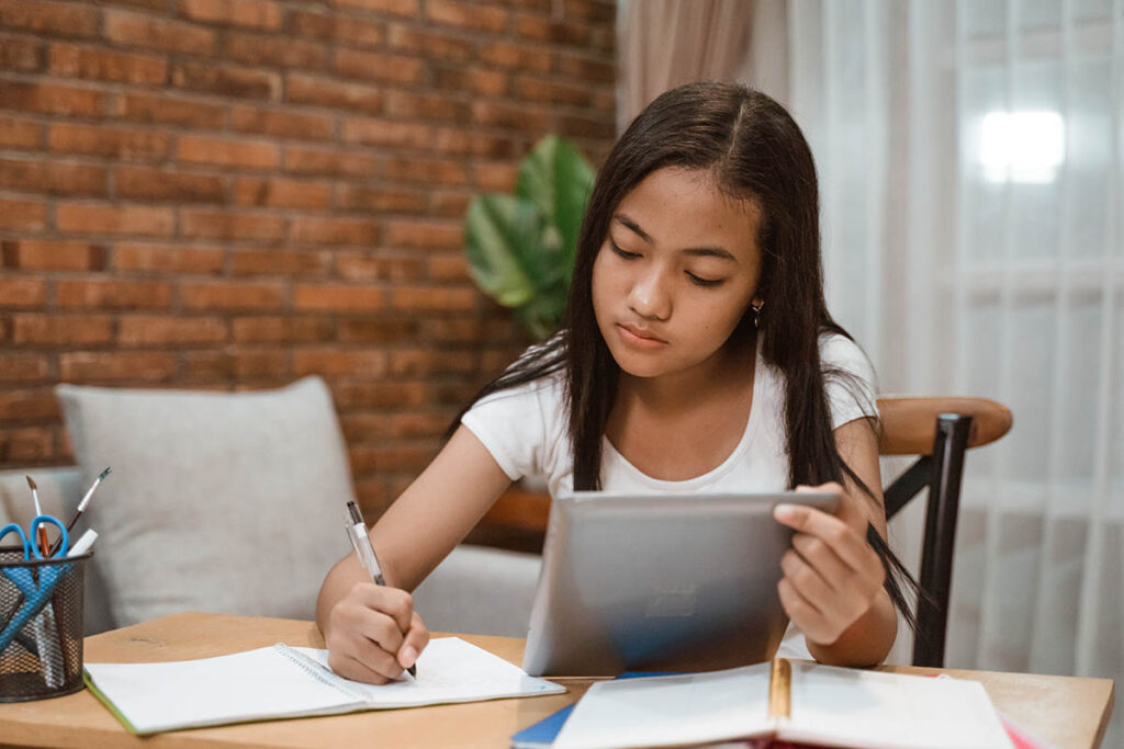 a teen looks at a tablet and writes on a piece of paper while learning about OCD