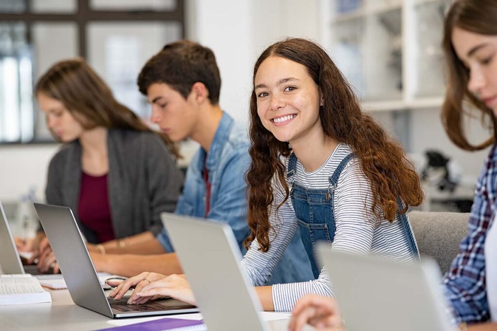 a row of teens sits on laptops and one smiles at the camera while looking up OCD help