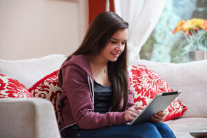 A teen looks at a tablet while sitting on a couch reading about OCD help