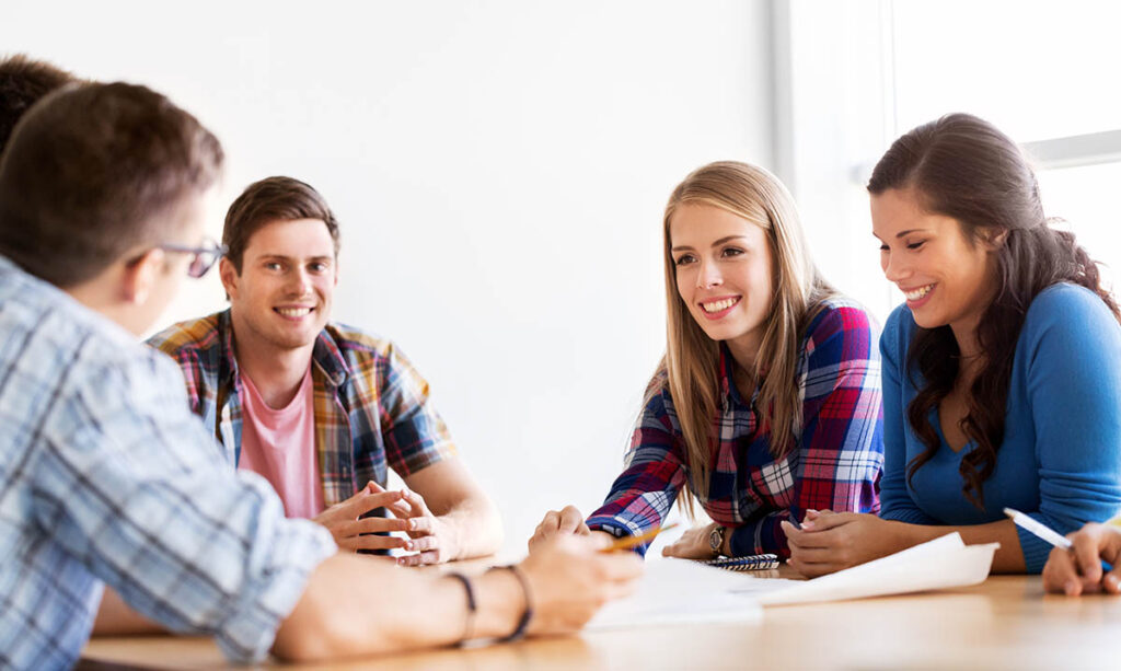 a group of young adults sit at a table with papers and pens and talk to each other about OCD treatment