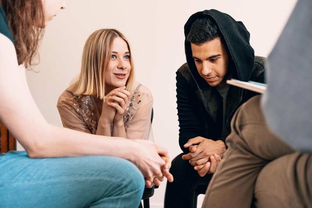 a group of young people sit in chairs and lean in to talk to each other about OCD treatment