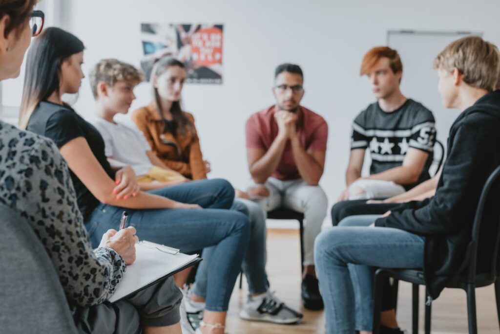 during depression treatment a group of young people sit in chairs and talk while a therapist listens