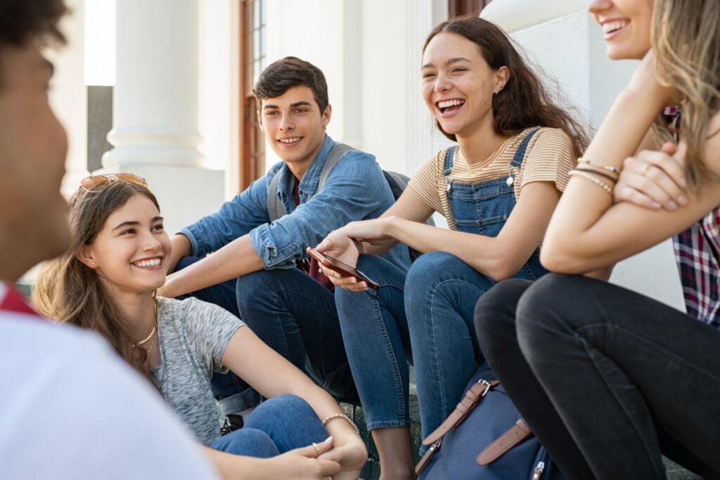 a group of young people sit outside and laugh and smile and talk about mental health treatment