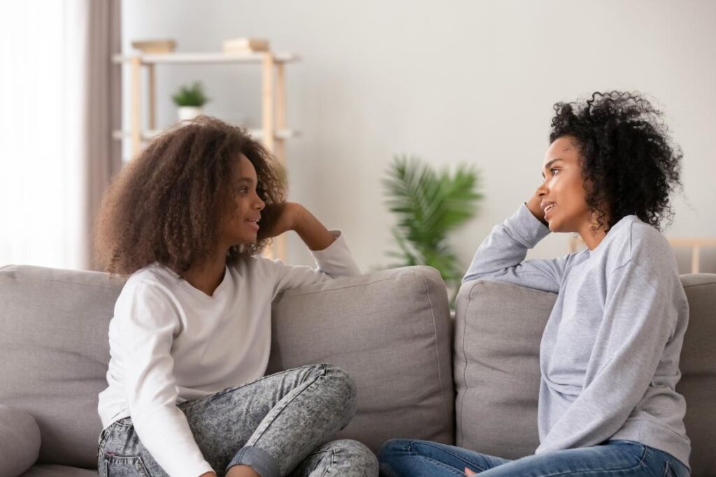 a young person and their parent sit on a couch facing each other and talk to each other about mental health treatment