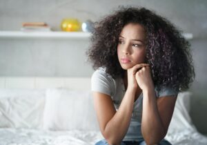 a young person looks sad while sitting in bed and looks off in need of trauma treatment