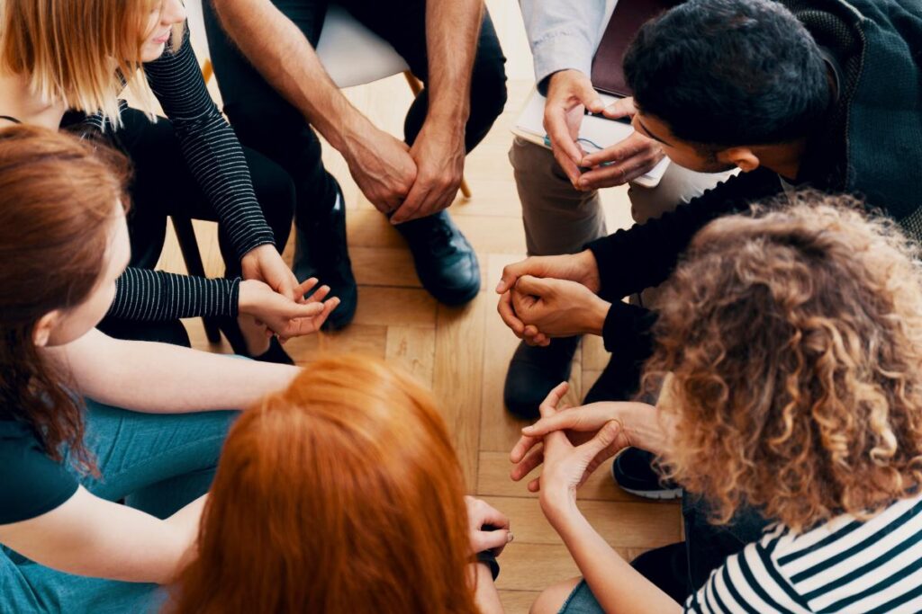 a group of people sit and talk and lean in during group therapy for trauma